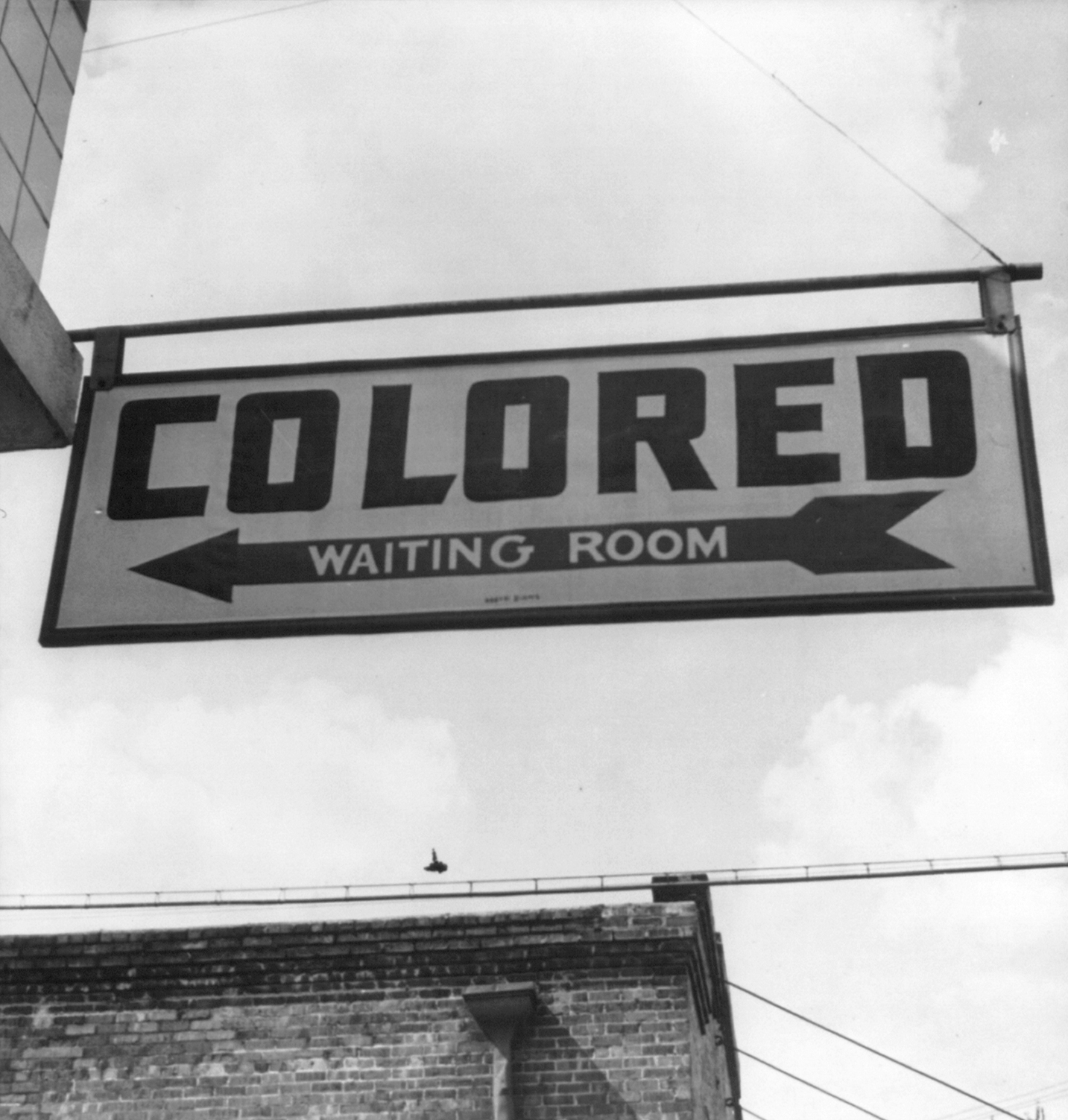 A sign that reads 'Colored Waiting Room' hangs from a building