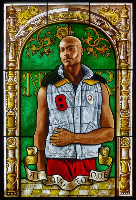 A brown-skinned man in a blue vest stands in front of a green arched window. His left arm is crossed over his abdomen.